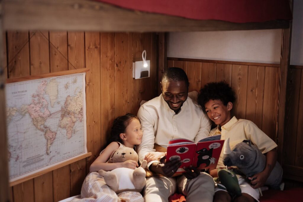 A father shares a bedtime story with his smiling children in a warm, cozy bedroom setting.